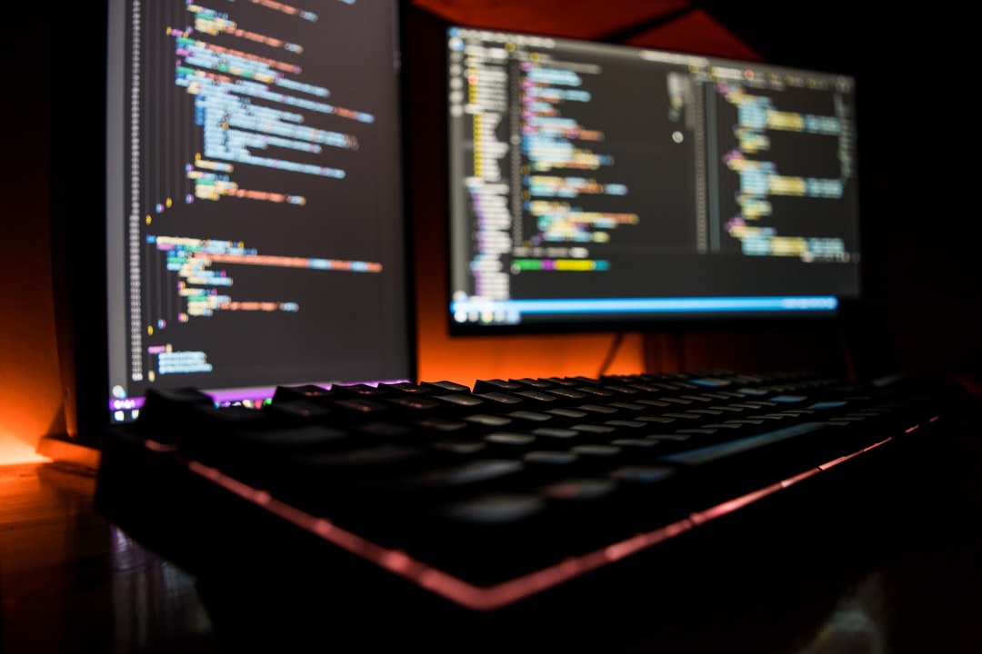 Programming code on a monitor with RGB keyboard in a dark setup.